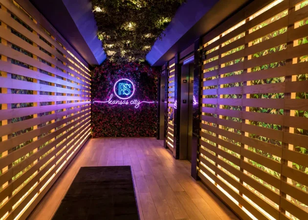 Interior hallway featuring a neon sign that reads 'Kansas City' and decorative greenery on the walls.