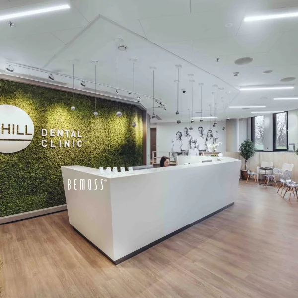 Reception area of Schill Dental Clinic featuring a green moss wall and modern white desk.