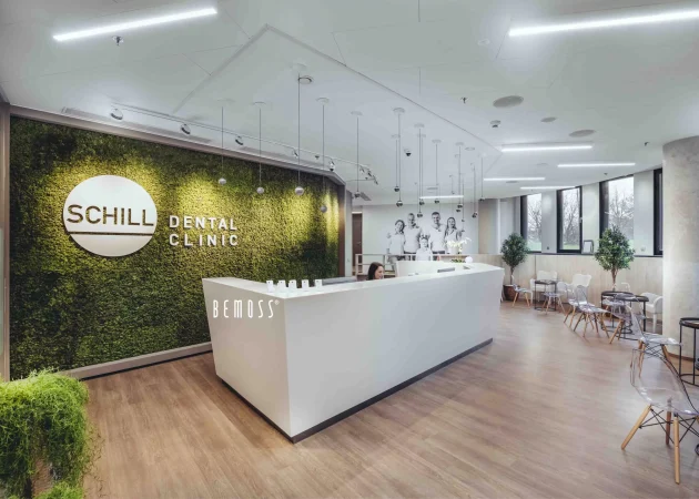 Reception area of Schill Dental Clinic featuring a green moss wall and modern white desk.