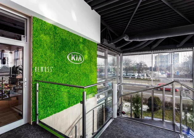 Kia logo displayed on a green wall in a modern indoor setting with glass railing.