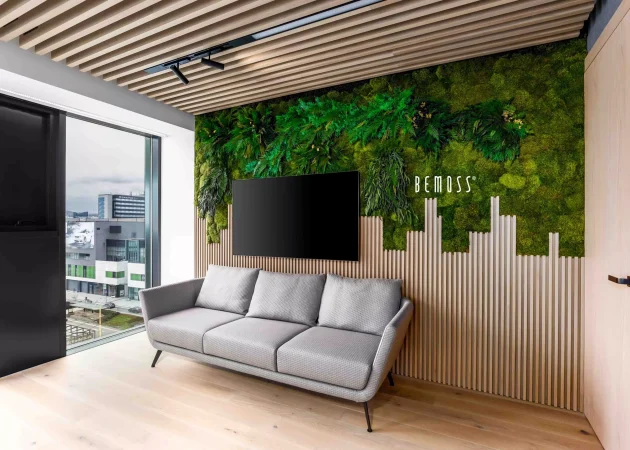 A modern living room featuring a gray sofa and a green moss wall art with the word 'BEMOSS'.