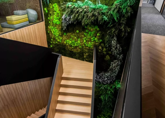 Interior staircase leading to a green wall with the Asseco logo and moss decoration.