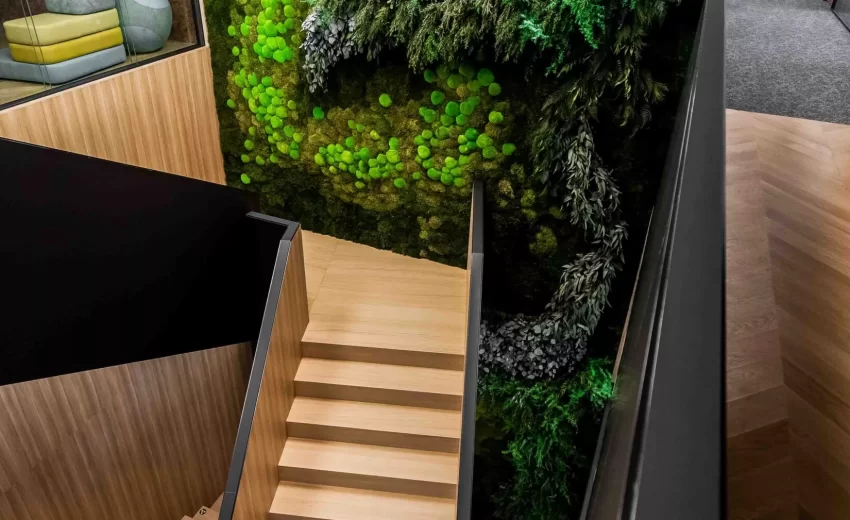 Interior staircase leading to a green wall with the Asseco logo and moss decoration.