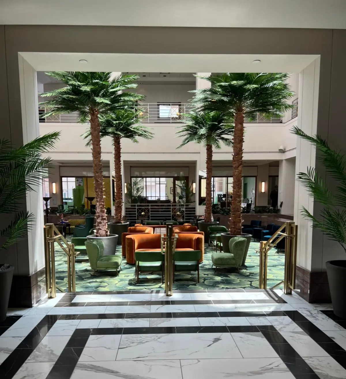Lounge area featuring palm trees and green and orange seating arrangements in a hotel lobby.