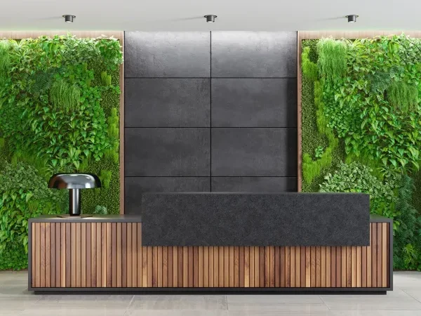 Reception desk made of wood with a dark panel and a green wall of plants behind it.