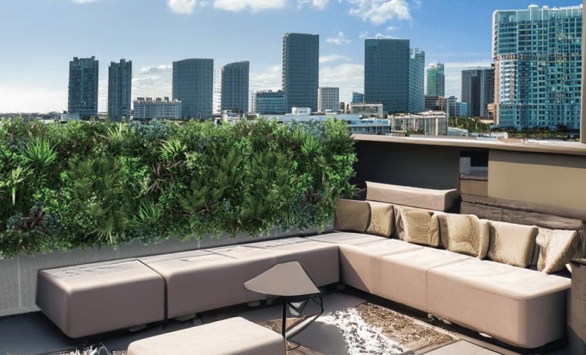 Stylish rooftop lounge area featuring modern furniture and greenery overlooking a city skyline with skyscrapers.