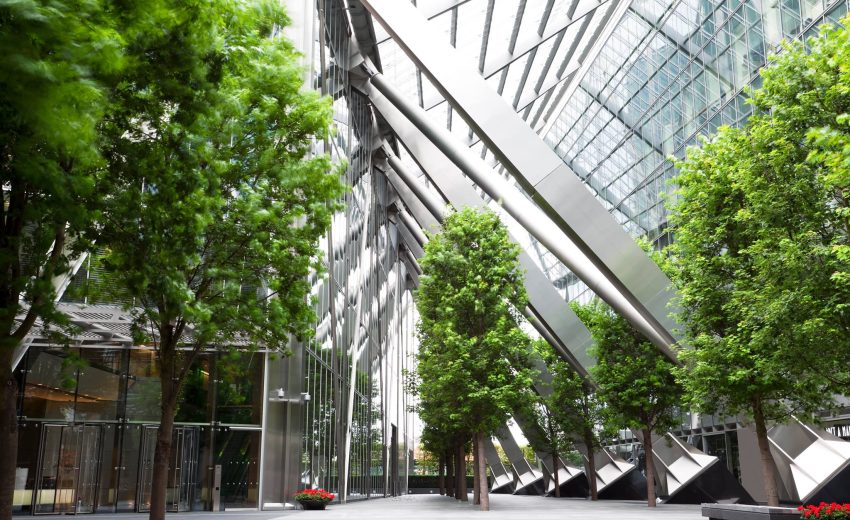 Contemporary architectural design featuring glass walls and trees, showcasing a blend of nature and modernity in an urban setting.