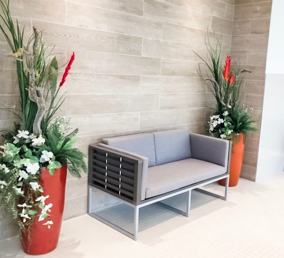 Contemporary gray sofa with black accents flanked by vibrant red planters and lush greenery in a stylish interior setting.