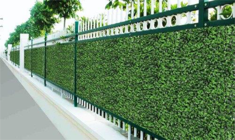 Artificial boxwood hedge panels mounted on a fence in a green color.