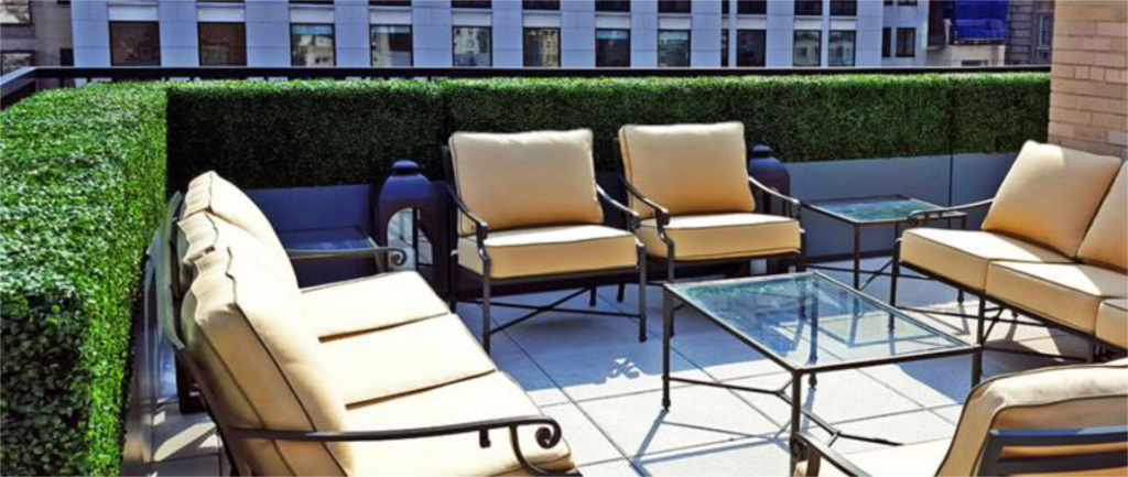 Seating area with beige cushions and a faux boxwood hedge on a rooftop terrace.