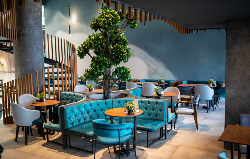 Contemporary restaurant seating area featuring teal upholstered booths, wooden tables, and a decorative indoor tree.