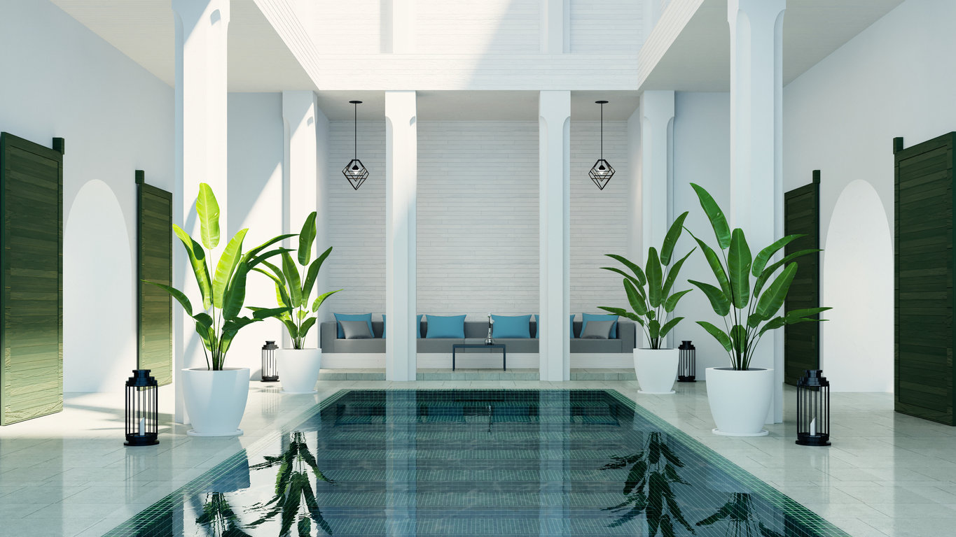 Indoor spa pool surrounded by replica plants in white pots and seating area with blue cushions.