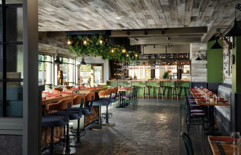 Custom hanging replica plants cascading above a contemporary bar in a stylish restaurant, with warm lighting, green accents, and wood textures