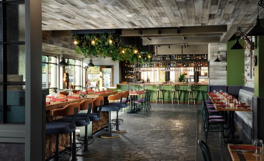 Custom hanging replica plants cascading above a contemporary bar in a stylish restaurant, with warm lighting, green accents, and wood textures