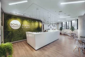 Reception area of Schill Dental Clinic featuring a green moss wall and modern white desk.