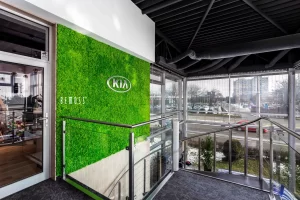 Kia logo displayed on a green wall in a modern indoor setting with glass railing.