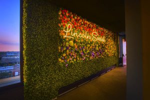 A vibrant floral wall with a neon sign that reads 'Lincoln Social' illuminated in warm light.