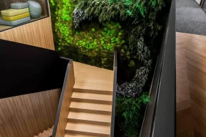 Interior staircase leading to a green wall with the Asseco logo and moss decoration.