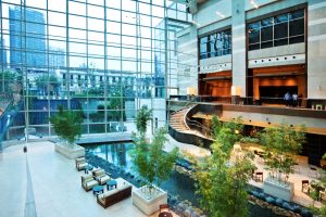 Interior view of a modern lobby featuring glass walls, seating areas, and a water feature with plants.